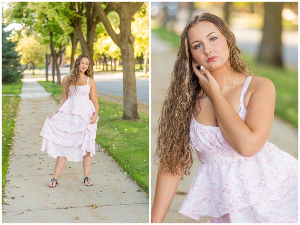 A young woman stands on a tree-lined sidewalk wearing a pink and white floral dress. She has curly hair and poses confidently with a thoughtful expression.