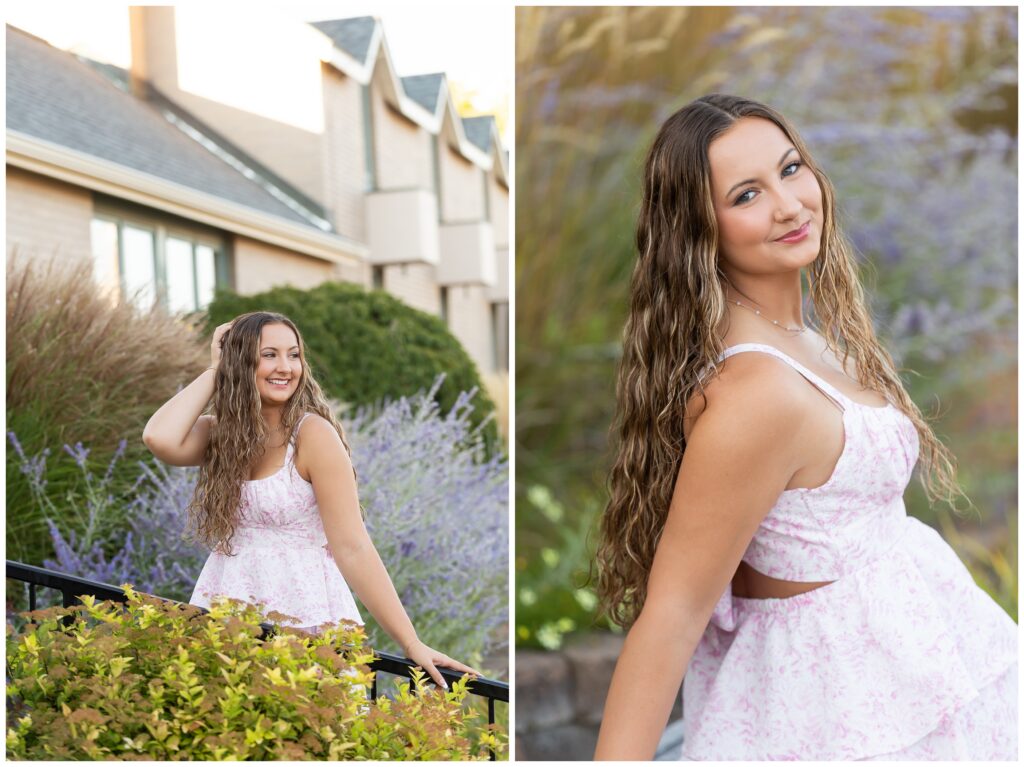 A woman in a white and pink floral dress stands near lush greenery and a building, smiling confidently. The mood is cheerful and serene.
