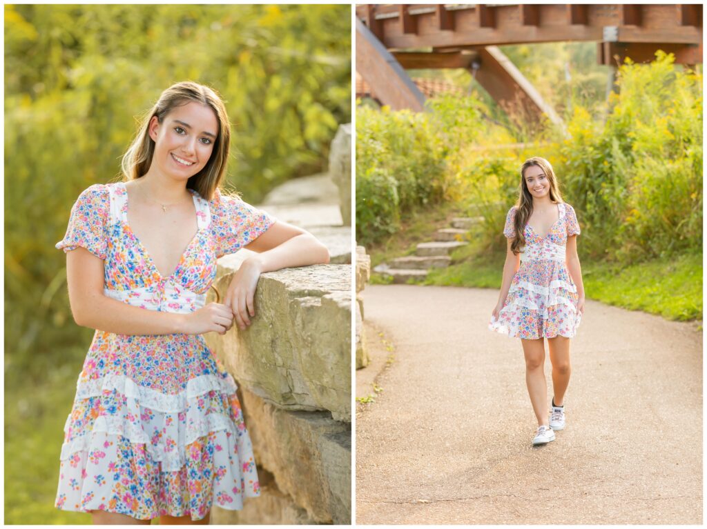 A young woman in a floral dress poses cheerfully in a sunny park. She leans on a stone wall and walks along a path under a rustic bridge.