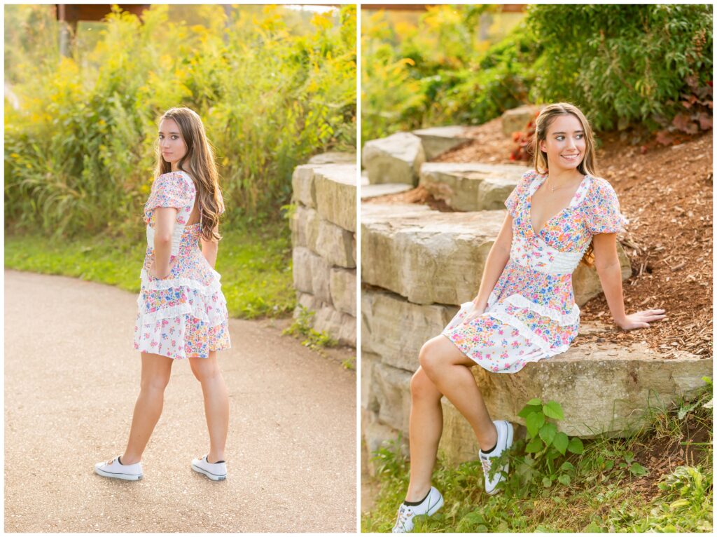 A woman in a floral dress poses in a sunny park. In one image, she stands on a path, gazing back confidently; in the other, she sits on a stone wall, smiling.