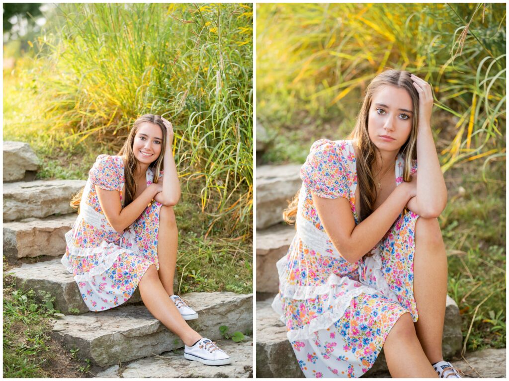 A young woman in a floral dress sits on stone steps, surrounded by tall grass. She looks pensively at the camera, with sunlight creating a warm glow.