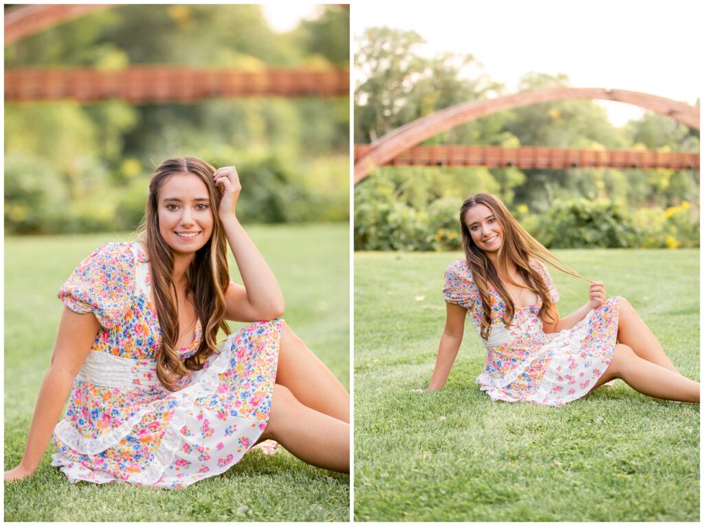Young woman sitting on grass, smiling, wearing a floral dress. Behind her, a wooden arch and green foliage suggest a serene park setting.