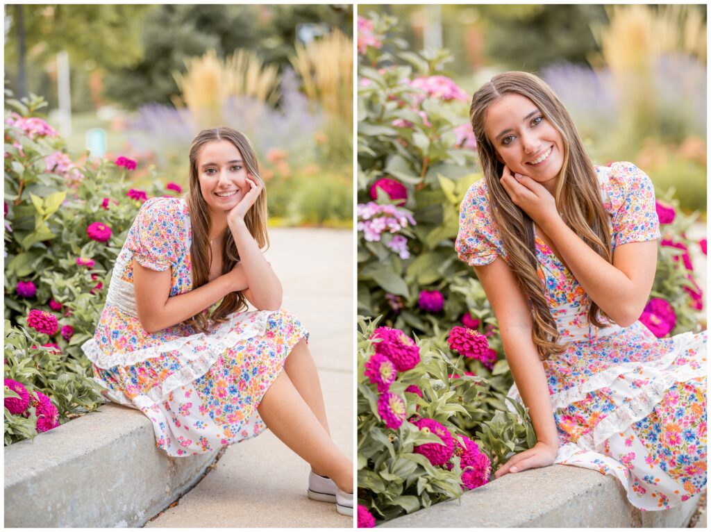 A young woman in a floral dress sits by vibrant pink flowers, smiling warmly. The lush greenery and soft focus background create a serene, joyful atmosphere.