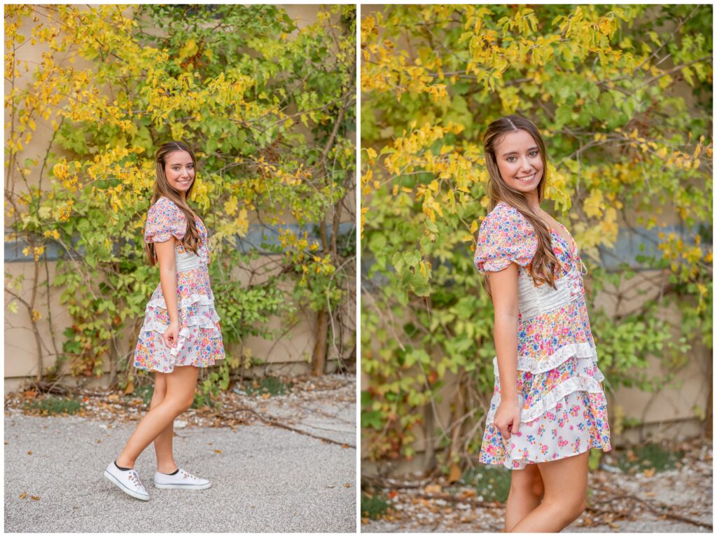 A young woman in a colorful floral dress stands on a path, surrounded by lush green and yellow foliage. She smiles warmly, conveying a joyful tone.