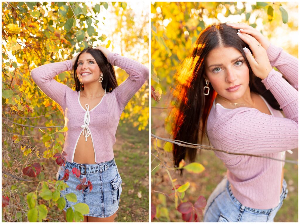 A woman with long brown hair, wearing a pink sweater and denim skirt, poses amidst colorful autumn foliage. She appears happy and relaxed.