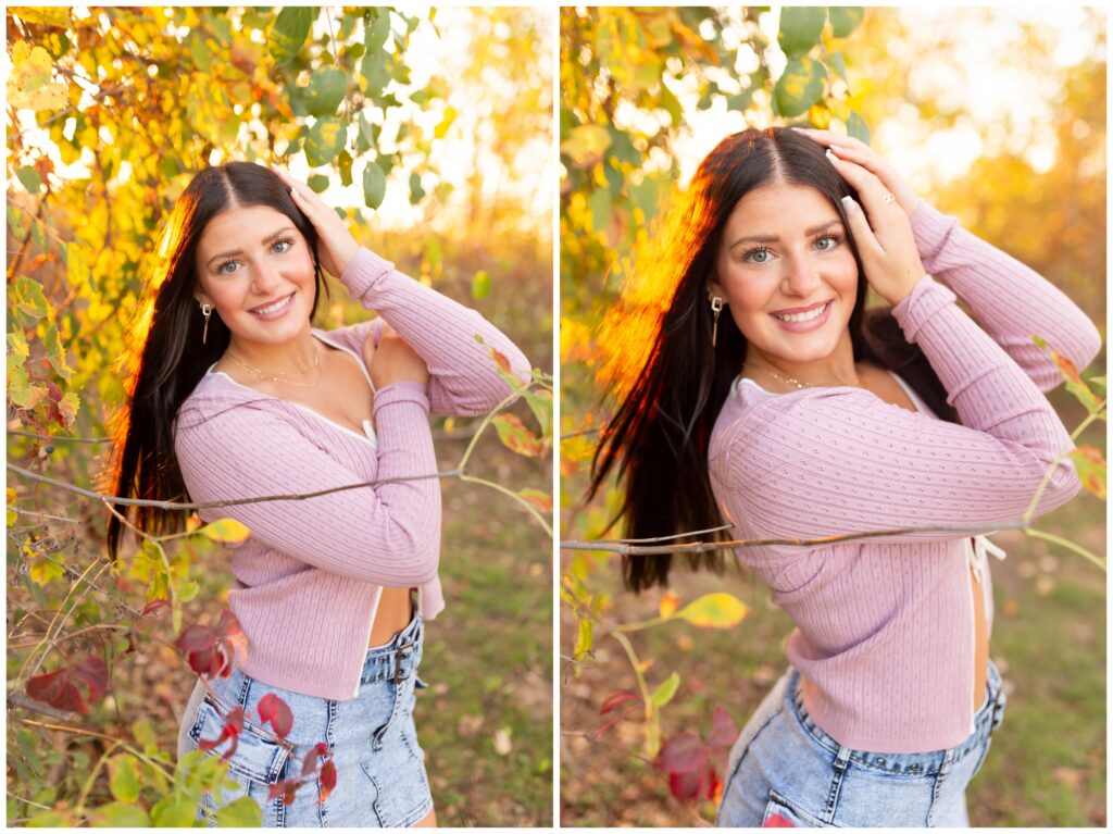 A woman with long dark hair and a pink sweater poses playfully among autumn leaves, smiling warmly. The sunlight creates a golden, dreamy background.