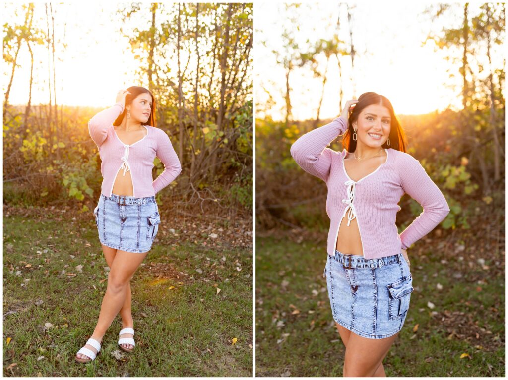A woman in a pink sweater and denim skirt poses outdoors during sunset. She stands confidently on grass with trees in the background, conveying a relaxed vibe.